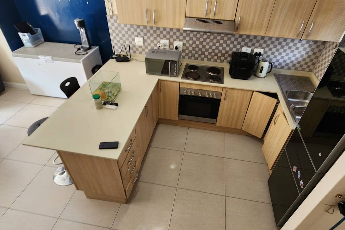 A functional U-shaped kitchen featuring light wood cabinetry, laminate countertops, integrated oven and hob, and a tiled backsplash, offering efficient workspace and storage.