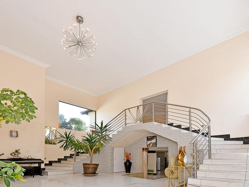 Spacious grand entrance hall featuring a sweeping staircase with stainless steel balustrades, high ceilings, and polished tiled flooring.
