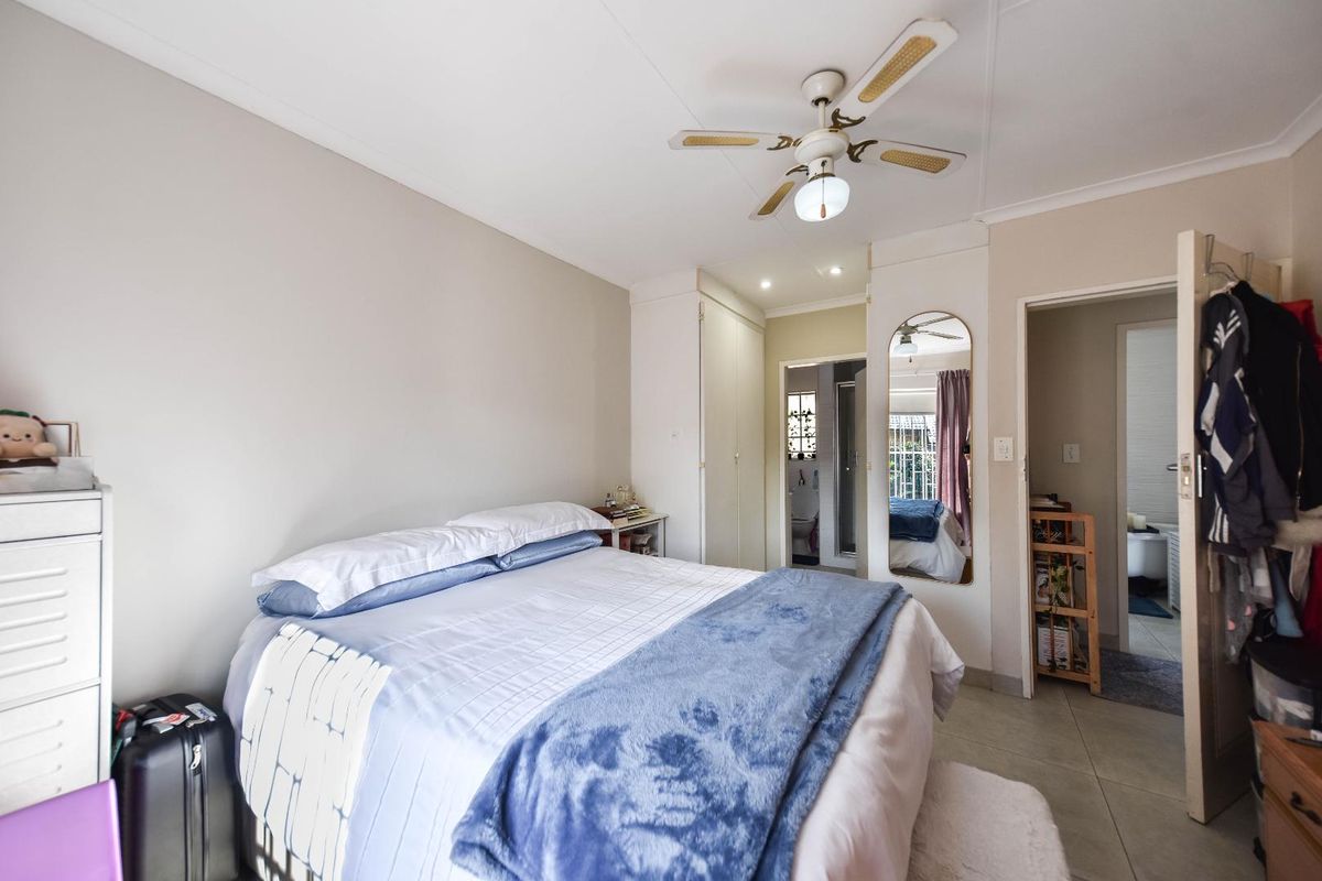 A bedroom featuring tiled flooring, a ceiling fan, and built-in cupboards, with an adjoining bathroom visible through the doorway.
