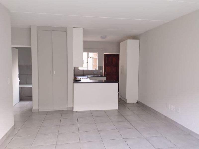 An open-plan living and kitchen area featuring neutral tiled flooring, built-in cabinetry, and a functional kitchen layout with a breakfast counter.