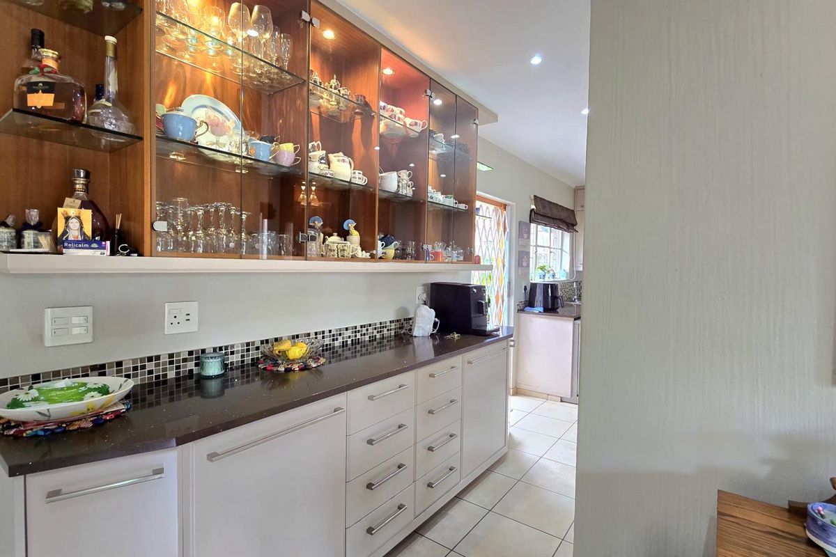 A well-maintained kitchen area featuring built-in cabinetry, glass-front display cupboards with integrated lighting, and a dark stone countertop with a mosaic tile backsplash.