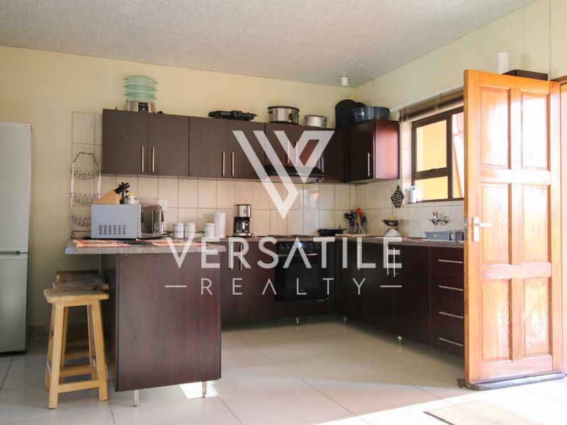 A functional kitchen featuring dark wood cabinetry, tiled backsplash, and tiled flooring, providing a practical layout for daily meal preparation.