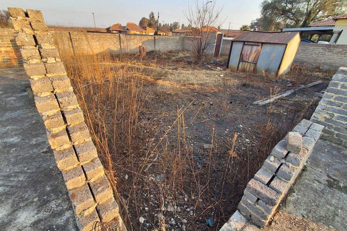 A vacant residential plot featuring a perimeter brick wall and a small metal storage shed, currently requiring significant landscaping and site clearance.