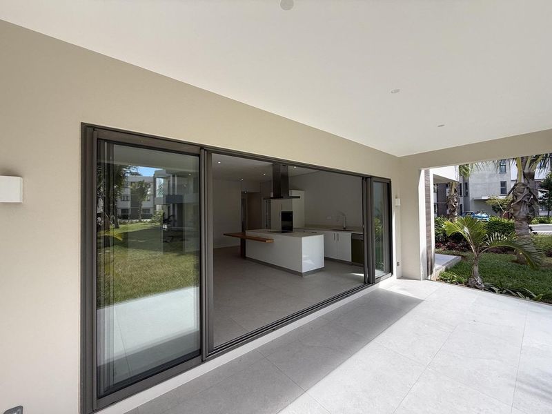 A modern covered patio featuring large sliding glass doors that open into a bright, open-plan kitchen area with tiled flooring throughout.