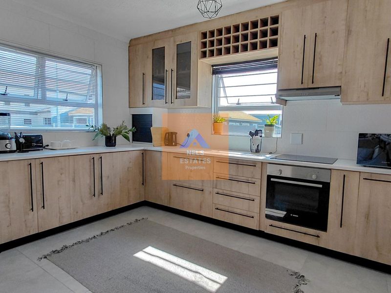 Modern kitchen featuring light wood-grain cabinetry, integrated appliances, sleek countertops, and ample storage space with a functional layout.