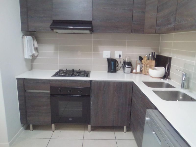 Modern kitchen featuring dark wood-grain cabinetry, stone countertops, a gas hob with extractor fan, and a double basin sink with tiled backsplash.