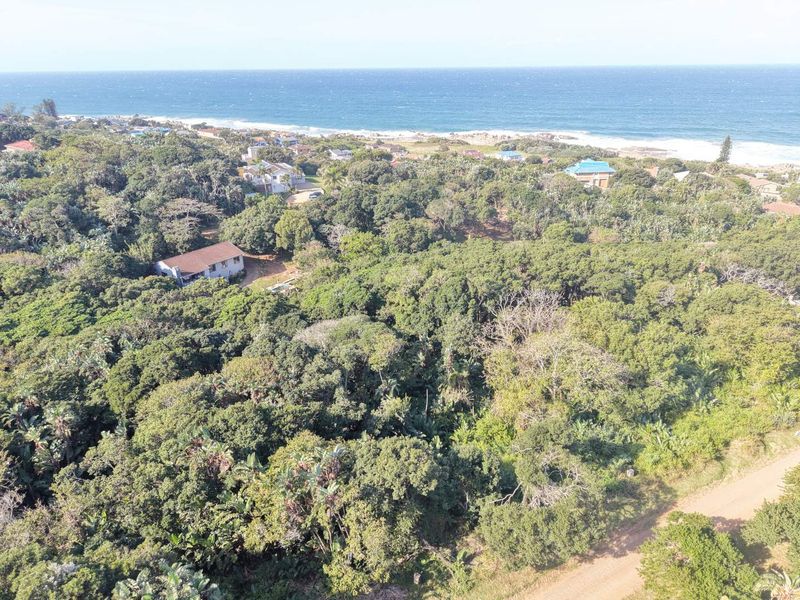 Aerial view of a densely wooded residential plot situated near the coastline, featuring natural vegetation and access to a nearby dirt road.