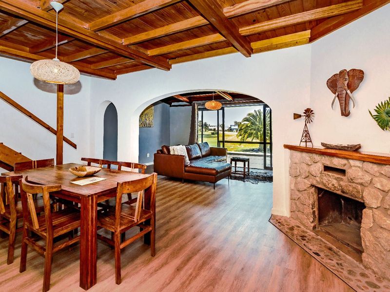 Open plan living and dining area featuring a rustic stone fireplace, exposed timber beam ceiling, and direct access to an outdoor patio space.