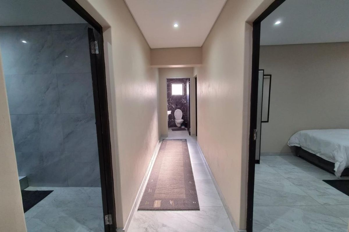 A clean, well-lit hallway featuring modern tiled flooring and recessed downlighting, providing access to adjacent rooms and a rear bathroom.