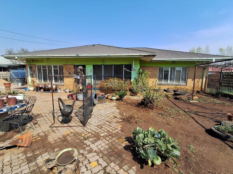 Rear view of a single-story house featuring a paved patio area, brick and painted facade, and security-barred windows.