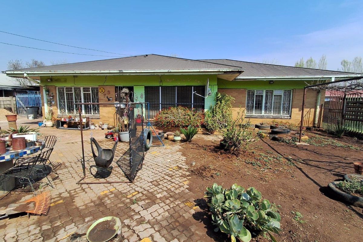 Rear view of a single-story house featuring a paved patio area, brick and painted facade, and security-barred windows.