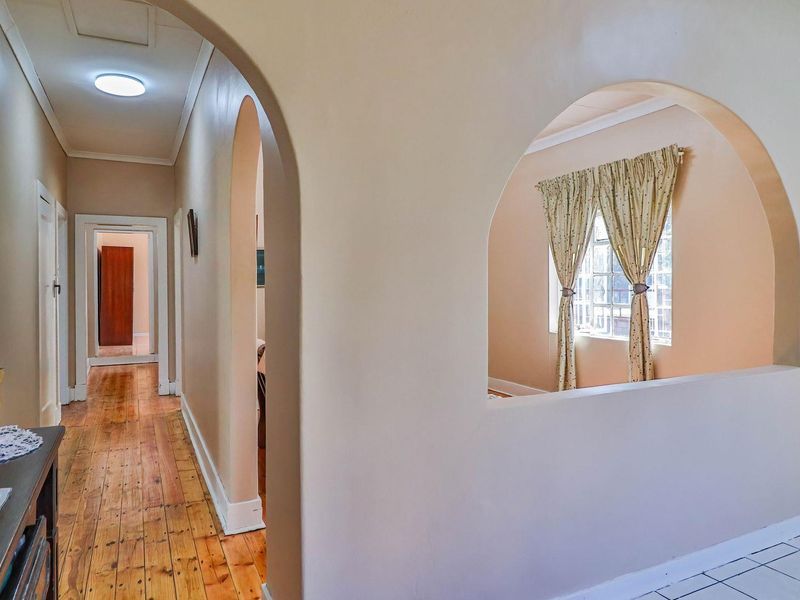 A bright hallway featuring an arched opening, polished hardwood floors, and a transition to tiled flooring, creating a spacious and connected layout.