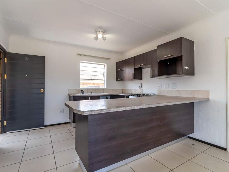 A clean, functional kitchen featuring dark wood cabinetry, laminate countertops, a gas hob, and tiled flooring in an open-plan layout.