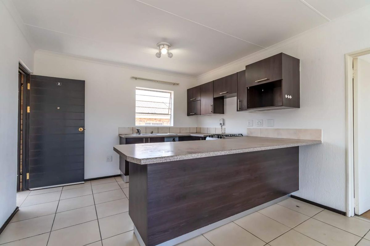 A clean, functional kitchen featuring dark wood cabinetry, laminate countertops, a gas hob, and tiled flooring in an open-plan layout.