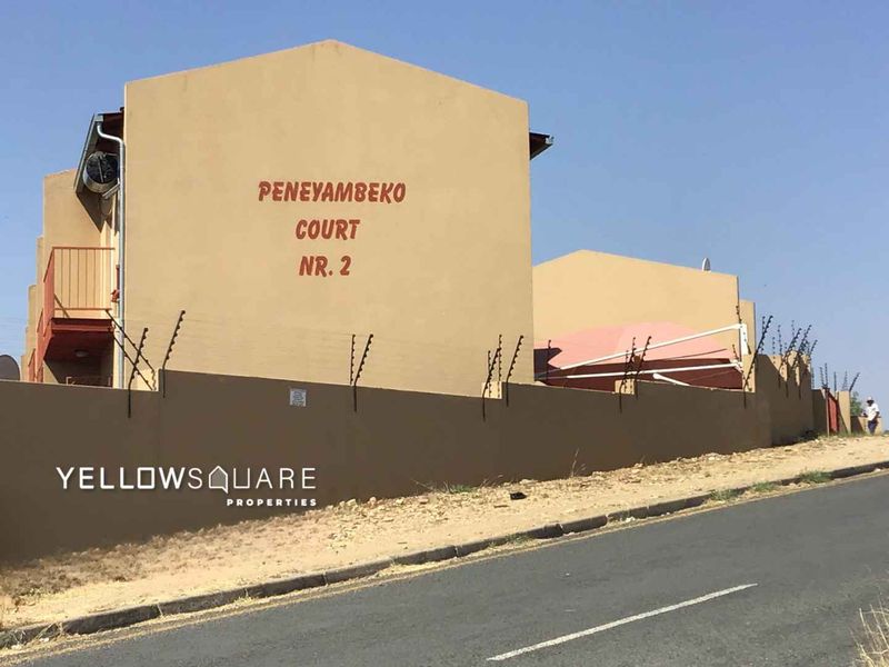 Street view of Peneyambeko Court townhouse complex featuring a perimeter wall with electric fencing and external building access.