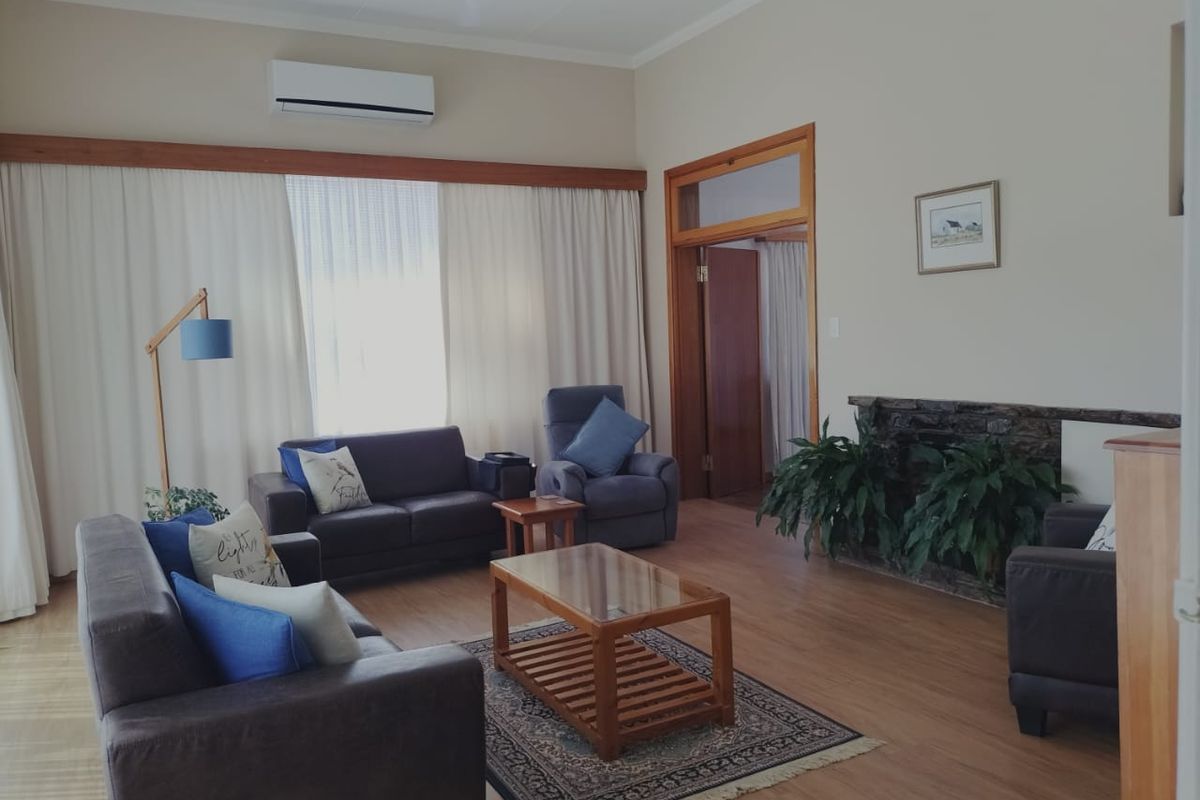 A spacious living room featuring wood-look flooring, a stone-clad fireplace, and a wall-mounted air conditioning unit.