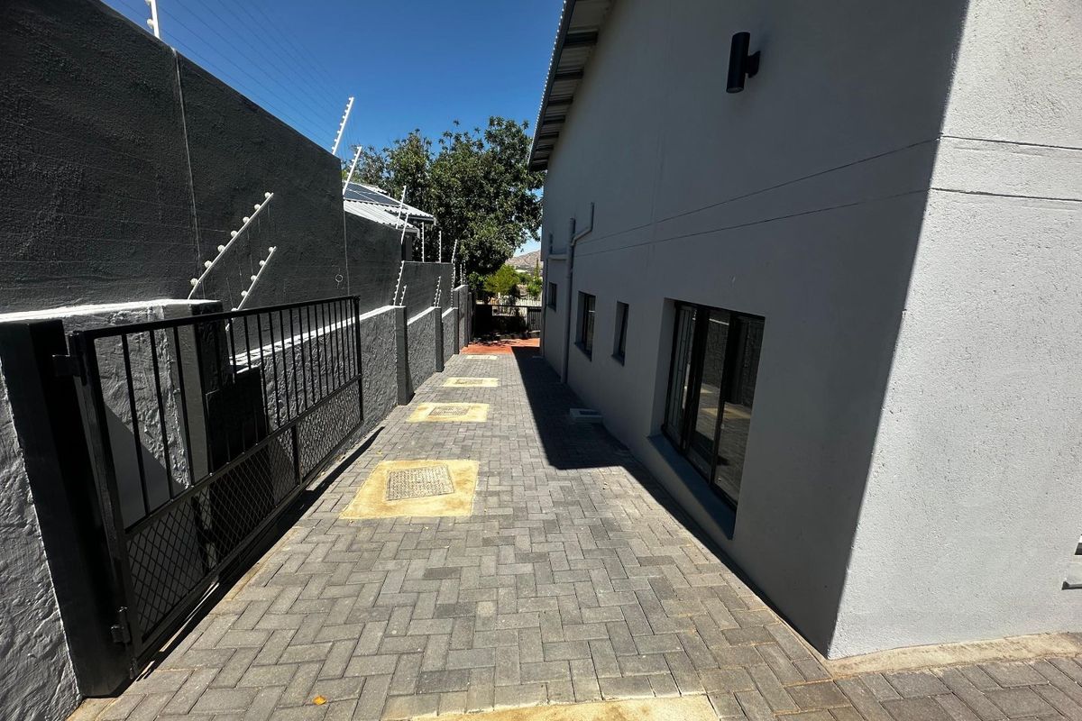 A clean, paved side passage featuring secure boundary walls with electric fencing and modern exterior wall lighting.