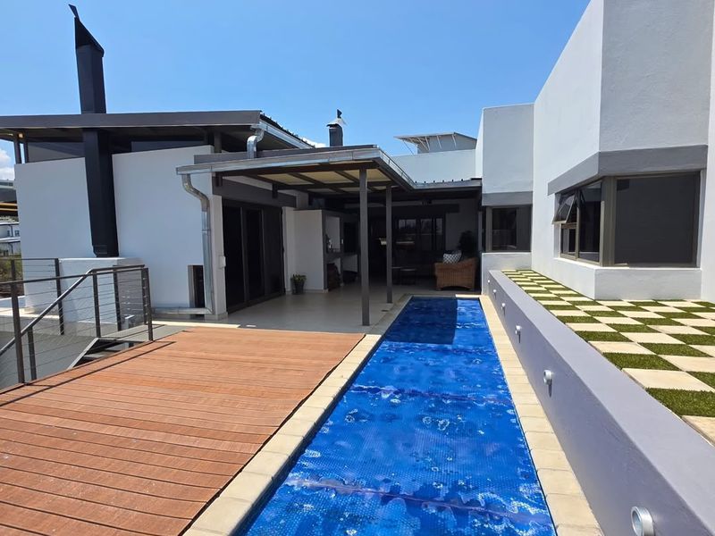 Modern outdoor entertainment area featuring a lap pool with cover, timber decking, and a covered patio with a built-in braai.