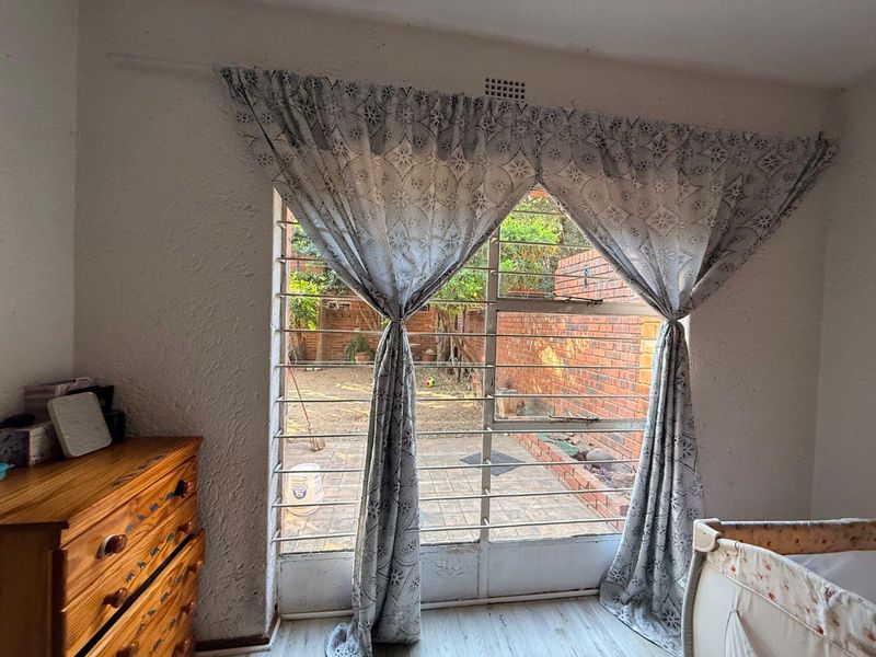 Bedroom featuring a large window with integrated steel security bars, overlooking a rear courtyard area with brick boundary walls.