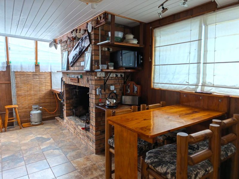 Covered patio area featuring a rustic brick fireplace, tiled flooring, and timber wall paneling, providing a cozy space for outdoor dining and relaxation.