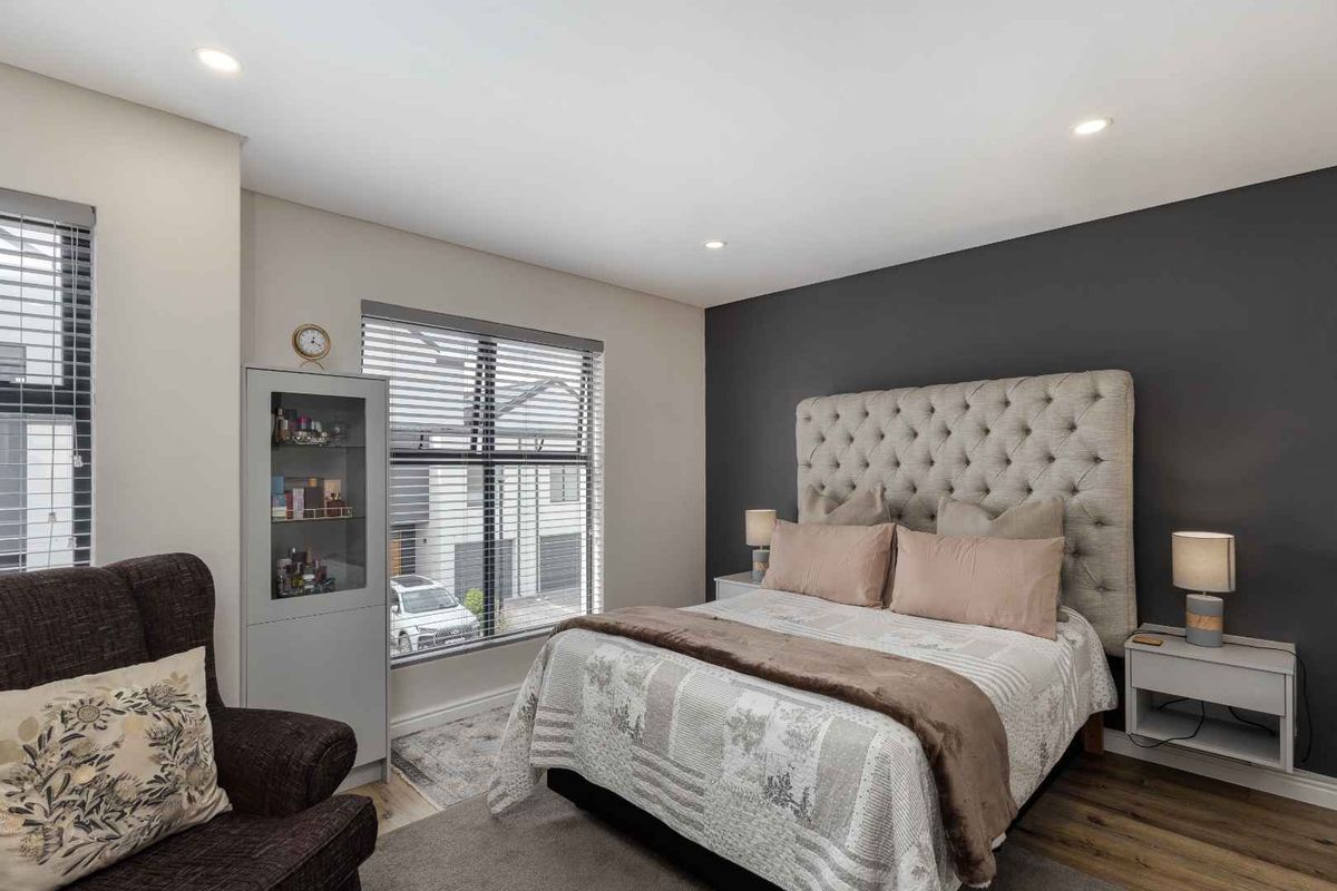 A well-maintained bedroom featuring recessed downlighting, modern laminate flooring, and a dark grey accent wall, providing a clean and contemporary living space.