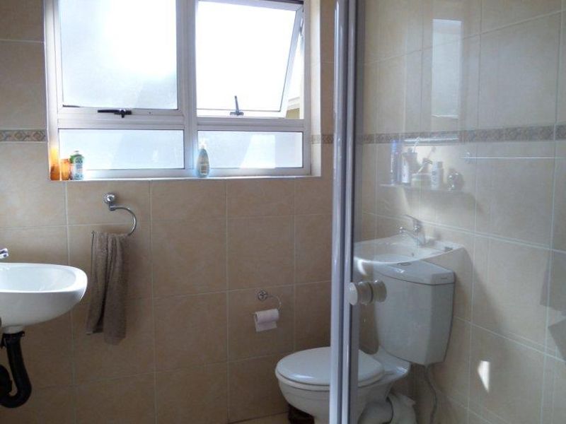 A functional bathroom featuring a shower enclosure, wall-mounted basin, toilet, and neutral tiled finishes throughout.
