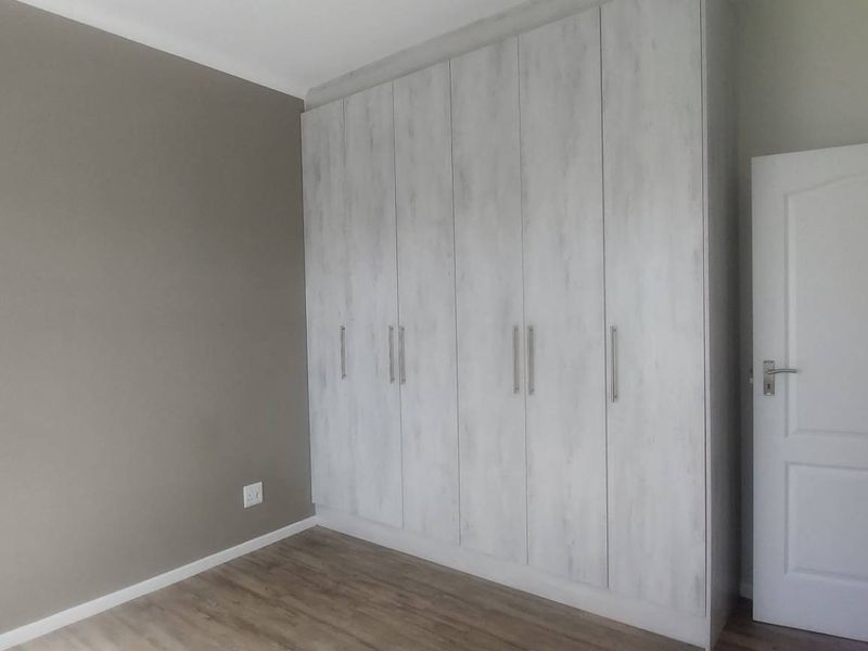 A clean, empty bedroom featuring modern light-wood finish built-in cupboards, neutral wall tones, and durable laminate flooring.