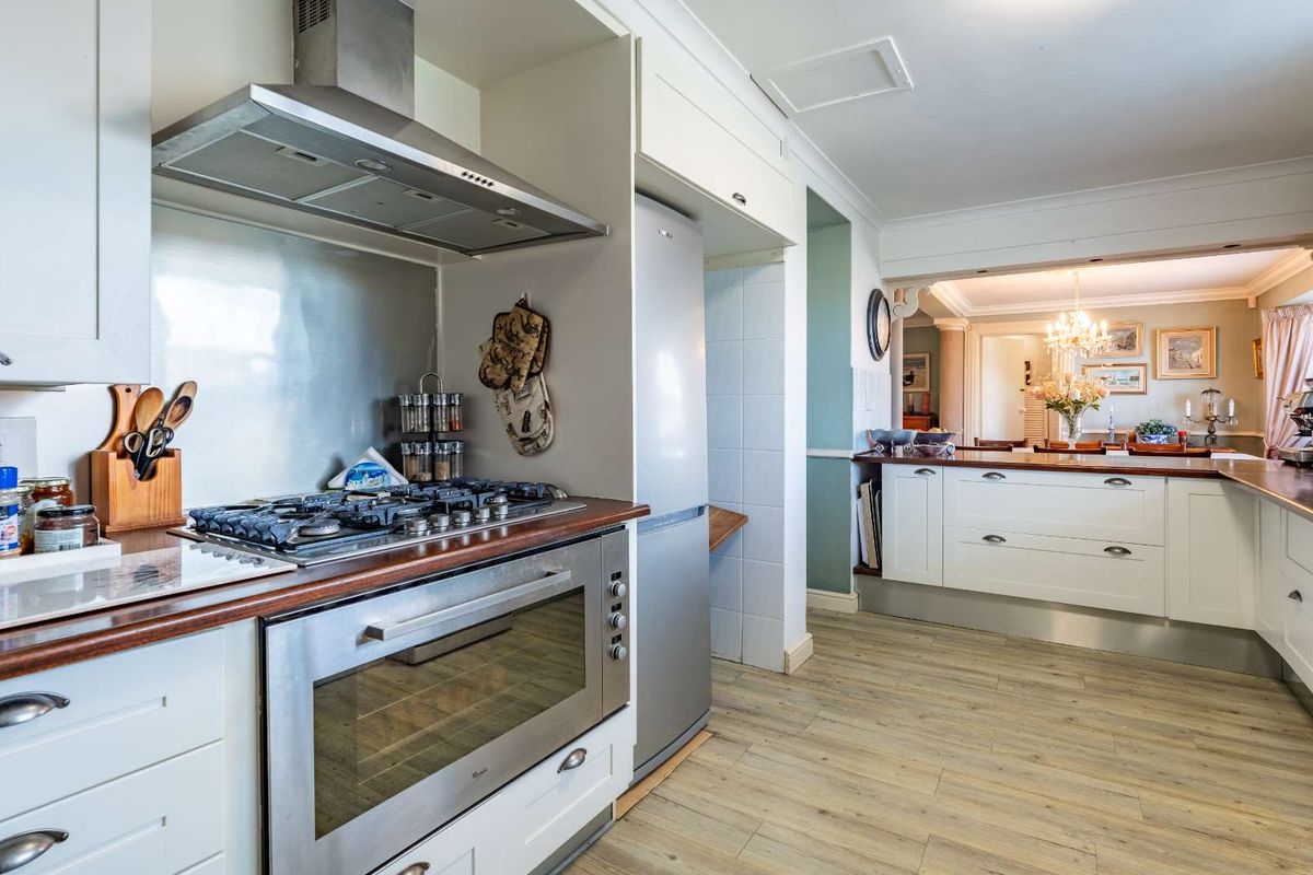 A well-appointed kitchen featuring a gas hob, stainless steel extractor fan, built-in oven, and wooden countertops, flowing into an adjacent dining area.