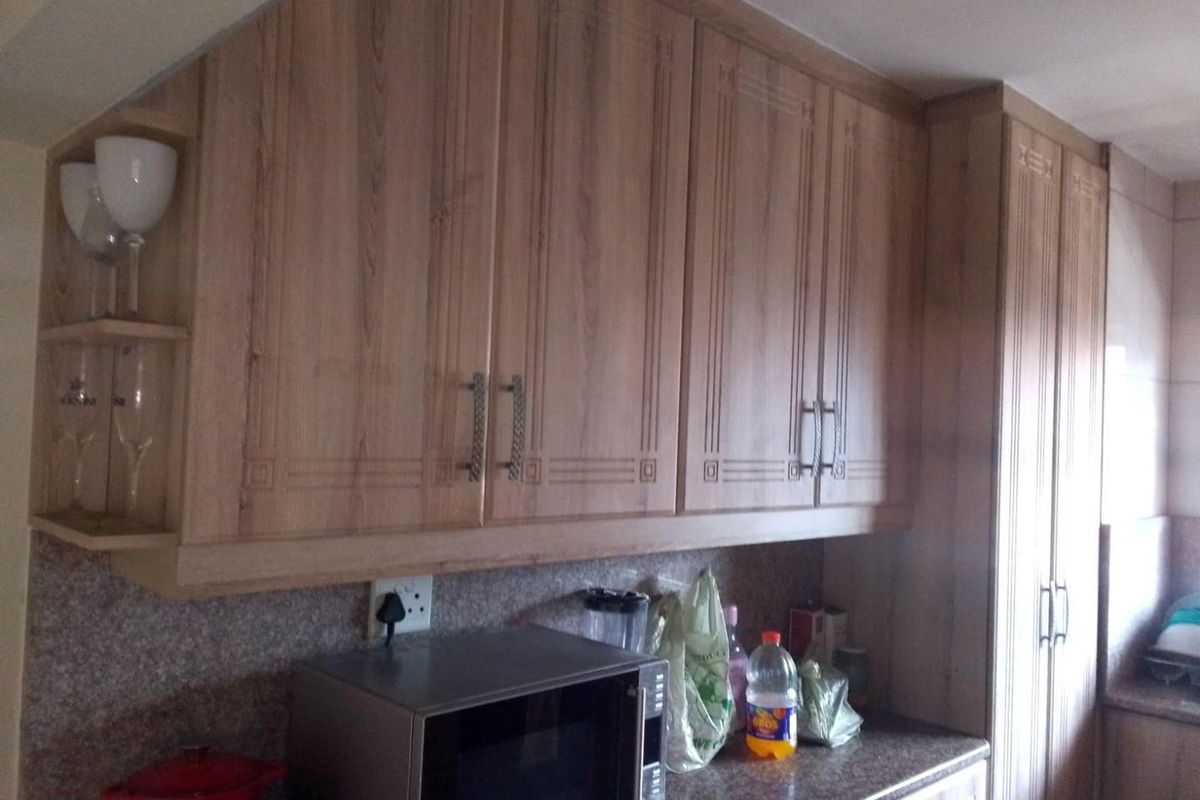 A kitchen area featuring wood-look laminate cabinetry, granite countertops, and built-in microwave space, offering functional storage and preparation surfaces.