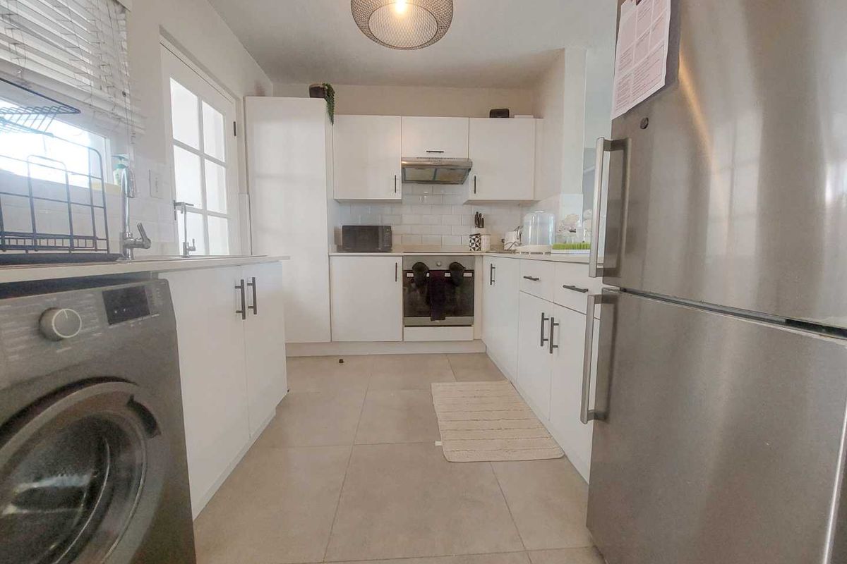 A functional kitchen featuring white cabinetry, subway tile backsplash, built-in oven, extractor fan, and tiled flooring with direct access to the exterior.