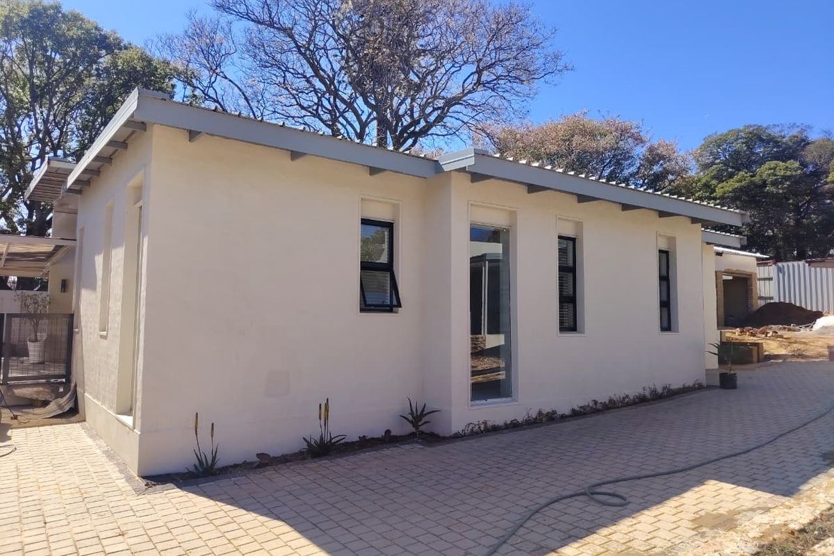Rear exterior view of the townhouse featuring plastered walls, modern aluminium window frames, and a paved driveway area.