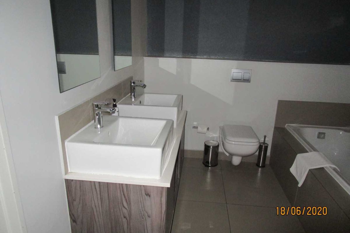 Modern bathroom featuring a double vanity with vessel sinks, a wall-mounted toilet, and a built-in bathtub with neutral tile finishes.