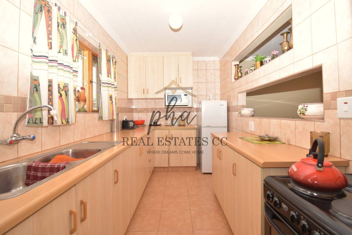 A functional galley-style kitchen featuring light wood-finish cabinetry, tiled walls, and a double-basin stainless steel sink.