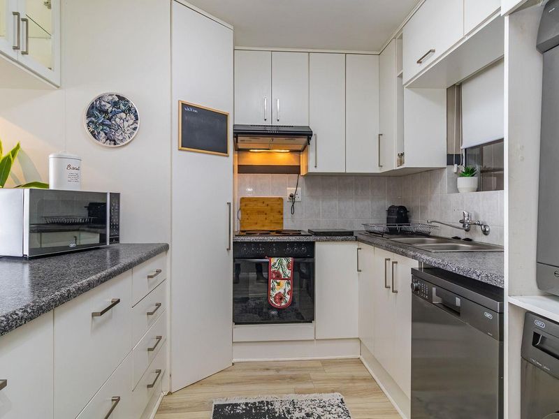 Compact kitchen featuring white cabinetry, granite-look laminate countertops, built-in oven and hob, and integrated laundry facilities with a tiled backsplash.