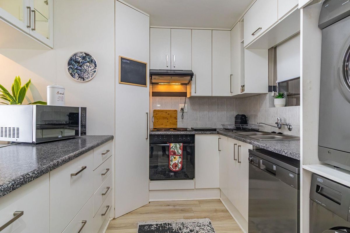 Compact kitchen featuring white cabinetry, granite-look laminate countertops, built-in oven and hob, and integrated laundry facilities with a tiled backsplash.