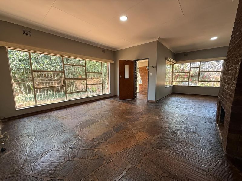 Spacious living room featuring unique flagstone flooring, a prominent brick fireplace, and large windows with security bars, offering a bright and open living space.