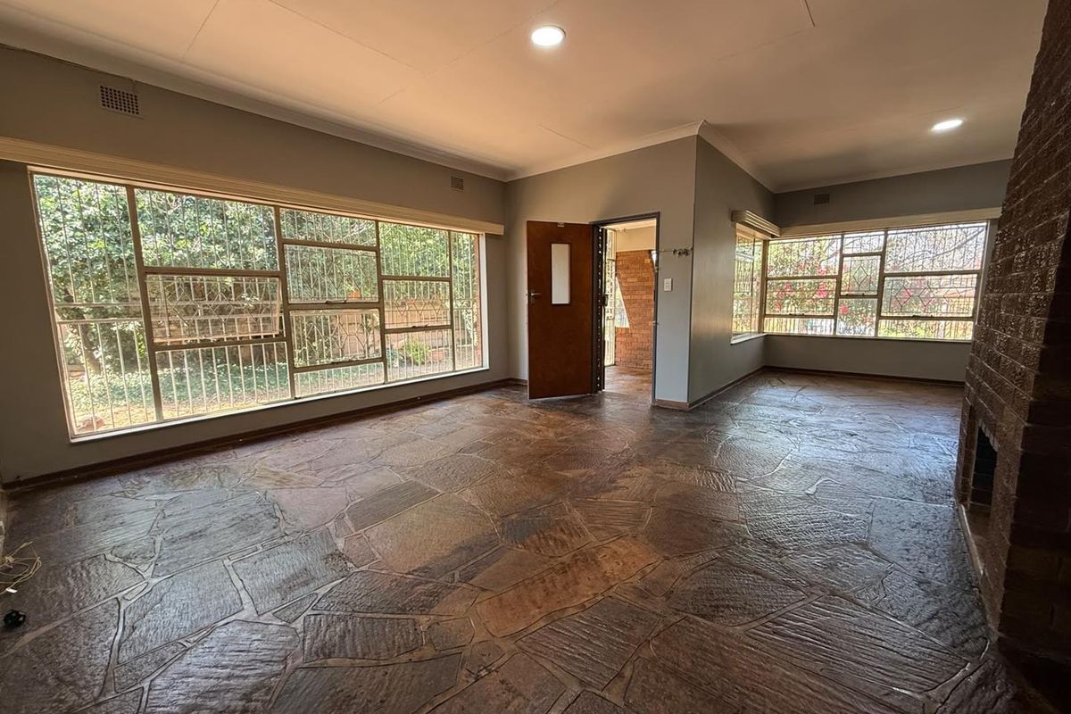 Spacious living room featuring unique flagstone flooring, a prominent brick fireplace, and large windows with security bars, offering a bright and open living space.