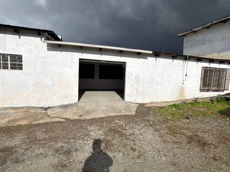 Rear exterior view of an industrial building featuring a large open bay entrance, concrete apron, and masonry walls with steel-framed windows.