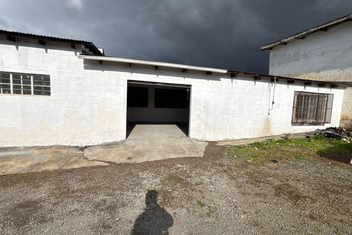 Rear exterior view of an industrial building featuring a large open bay entrance, concrete apron, and masonry walls with steel-framed windows.