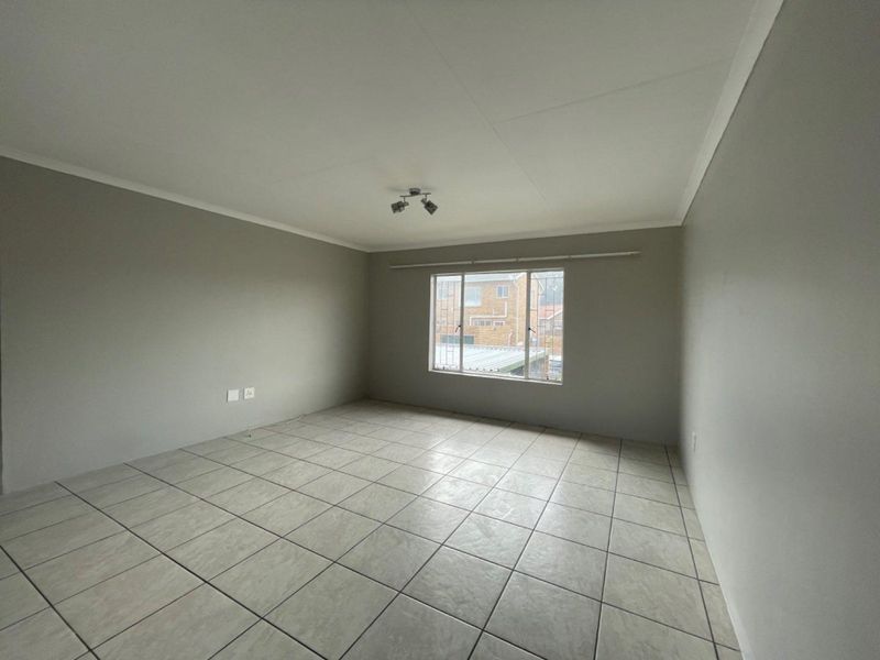A bright, empty living room featuring neutral grey walls, tiled flooring, and a window with security bars, offering a clean canvas for personalization.