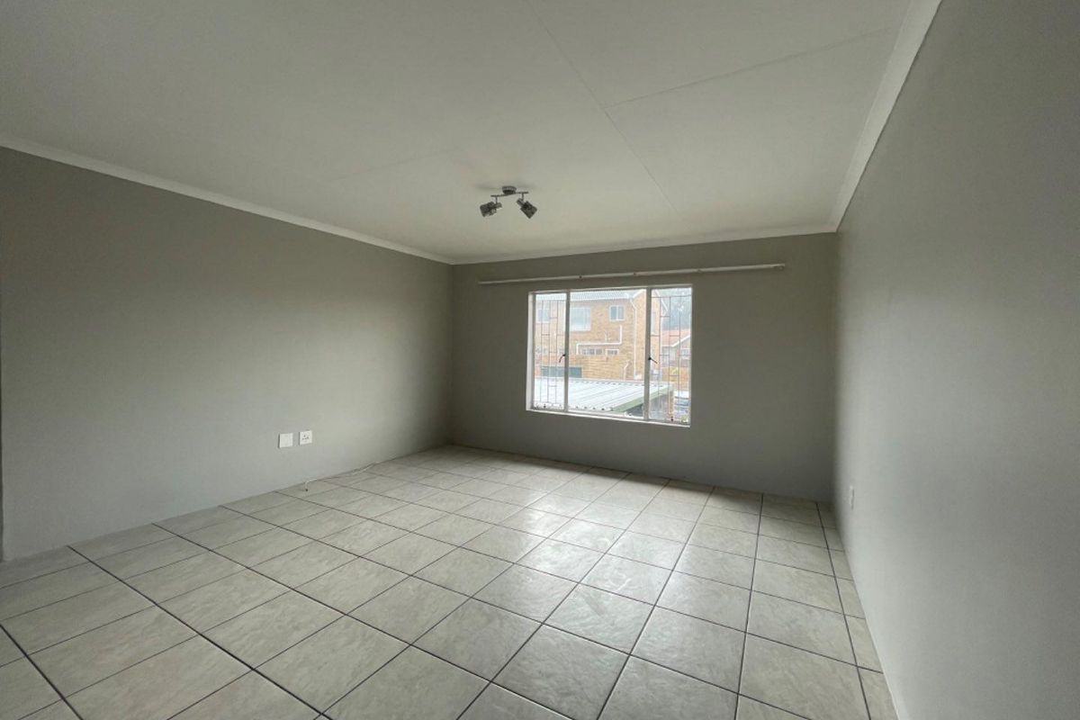 A bright, empty living room featuring neutral grey walls, tiled flooring, and a window with security bars, offering a clean canvas for personalization.