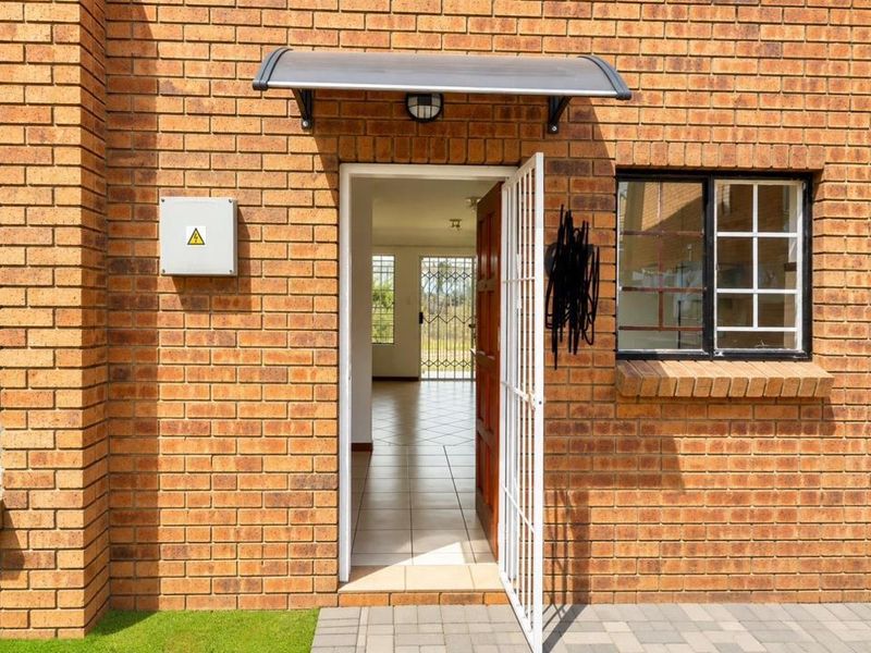 Front entrance of a brick apartment featuring a security gate, protective awning, and external electrical box, leading into an open-plan interior space.