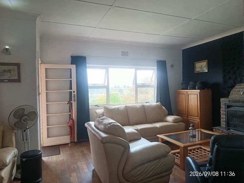 A living room featuring a brick fireplace, timber flooring, and large windows providing natural light.