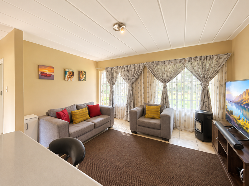 A comfortable living room featuring tiled flooring, a panelled ceiling, and large windows that allow for natural light.