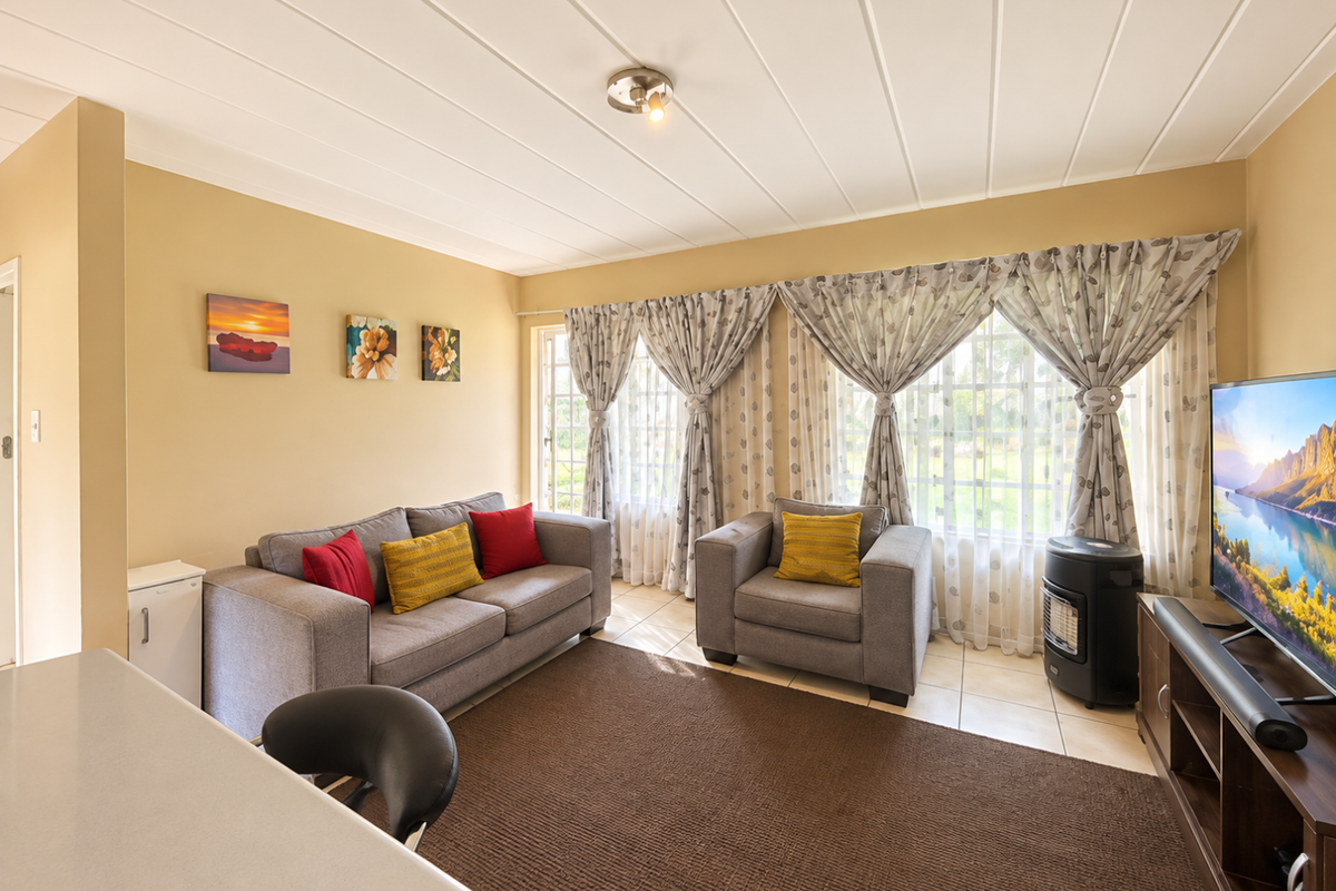 A comfortable living room featuring tiled flooring, a panelled ceiling, and large windows that allow for natural light.