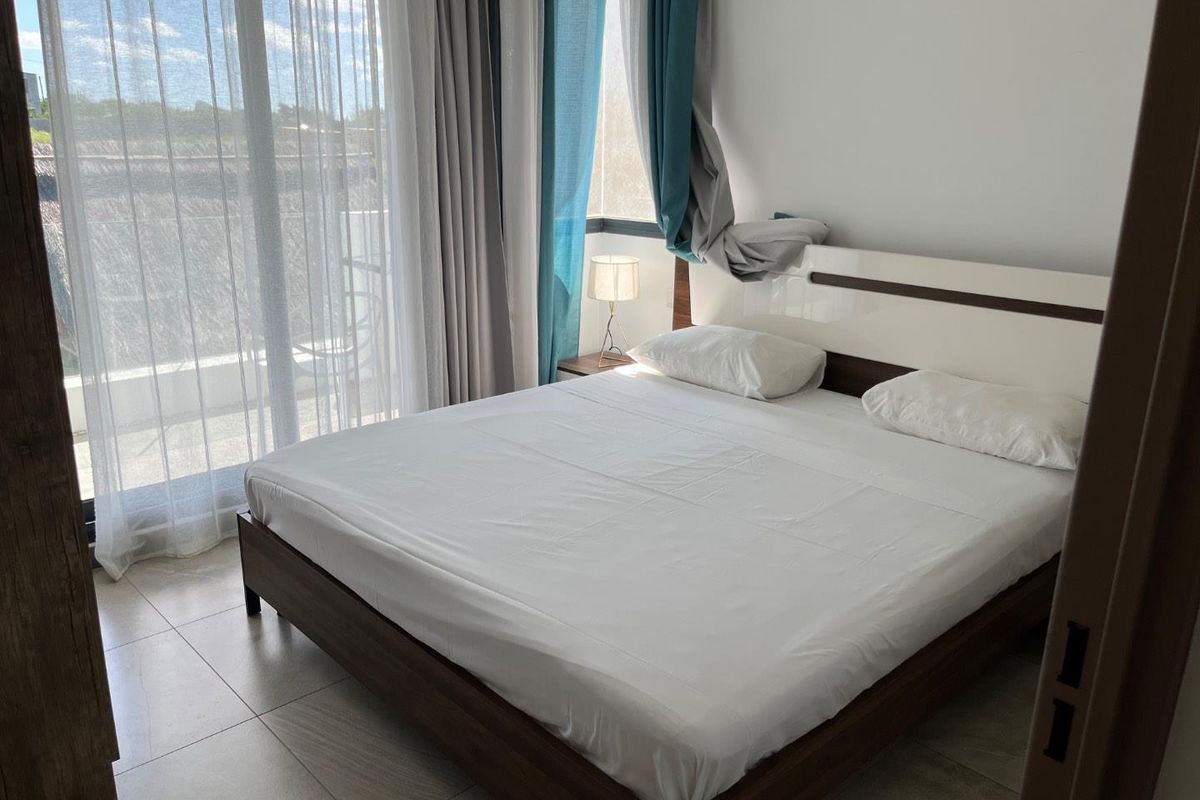 A bright bedroom featuring tiled flooring and a large sliding glass door providing access to an outdoor area.