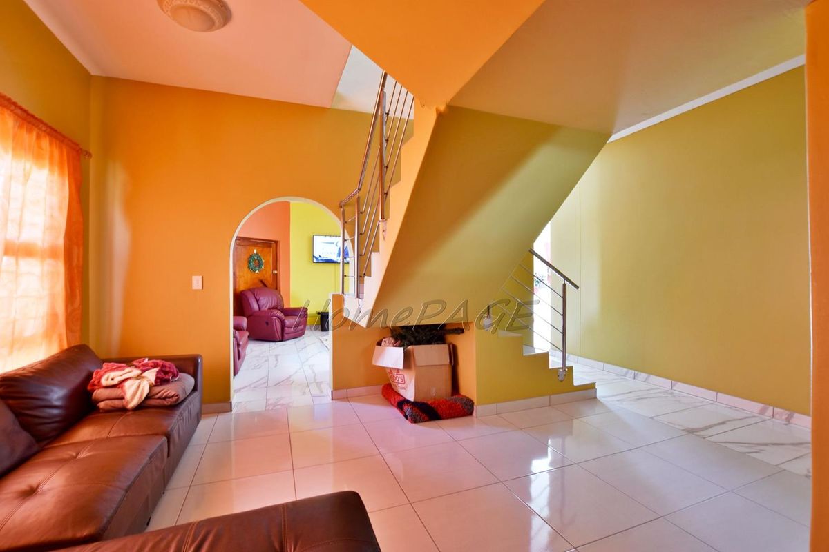 A living area featuring tiled flooring, an arched doorway leading to an adjacent room, and a staircase with a modern stainless steel balustrade.