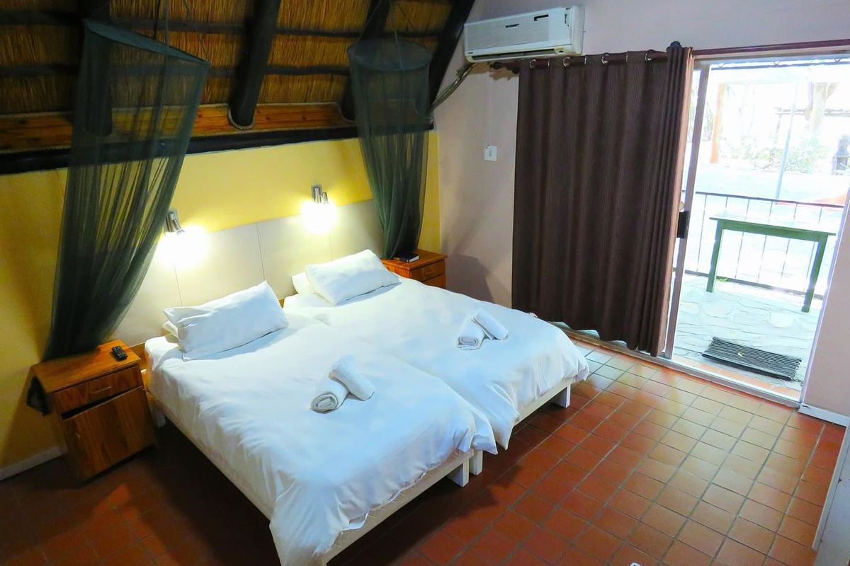 A bedroom featuring a traditional thatched roof with exposed timber beams, tiled flooring, and direct access to an outdoor patio through a sliding glass door.