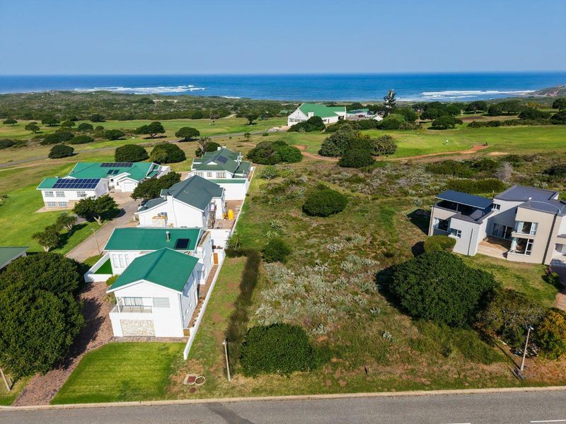 Aerial view of a vacant residential plot situated in a coastal estate, featuring proximity to the ocean and established neighboring properties.