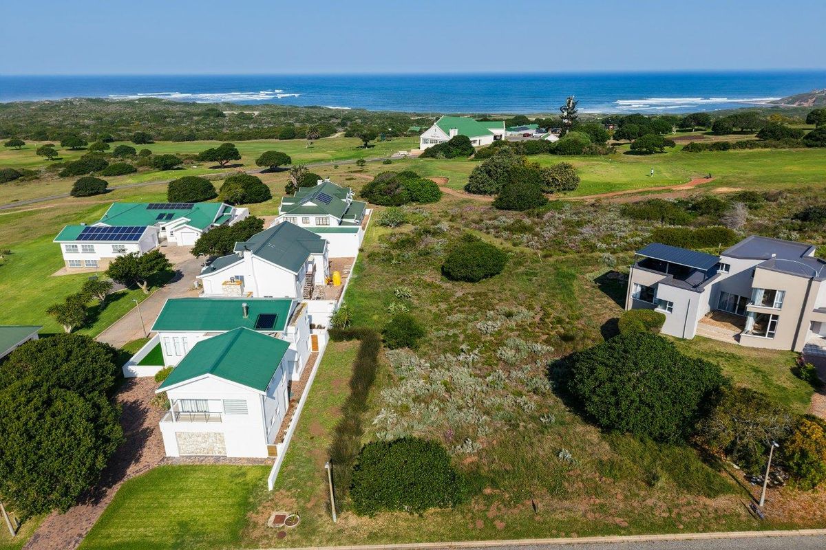 Aerial view of a vacant residential plot situated in a coastal estate, featuring proximity to the ocean and established neighboring properties.
